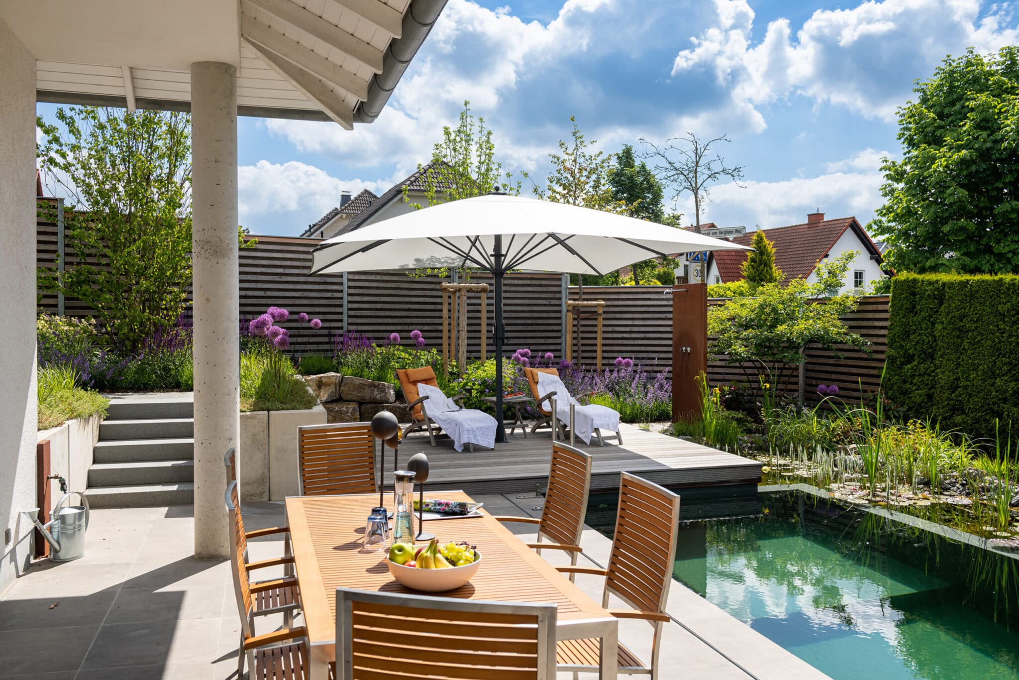 20220602_GvE_TSC6413-s Gartenbereich mit einem Tisch, Stühlen, einem Sonnenschirm und einem Pool in einem modernen Wohnumfeld.