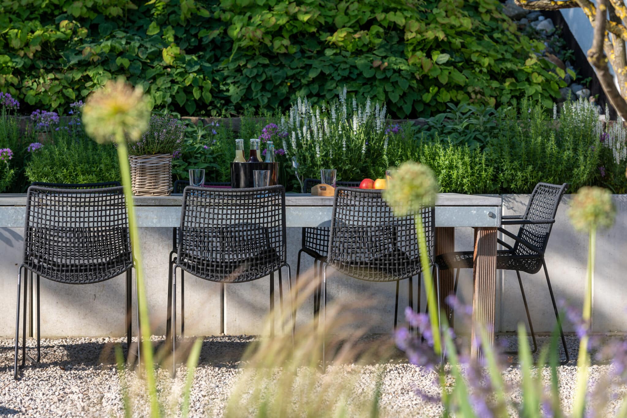 GvE Klute Schwarze Stühle an einem Tisch im Garten mit Pflanzen und Getränken im Hintergrund.