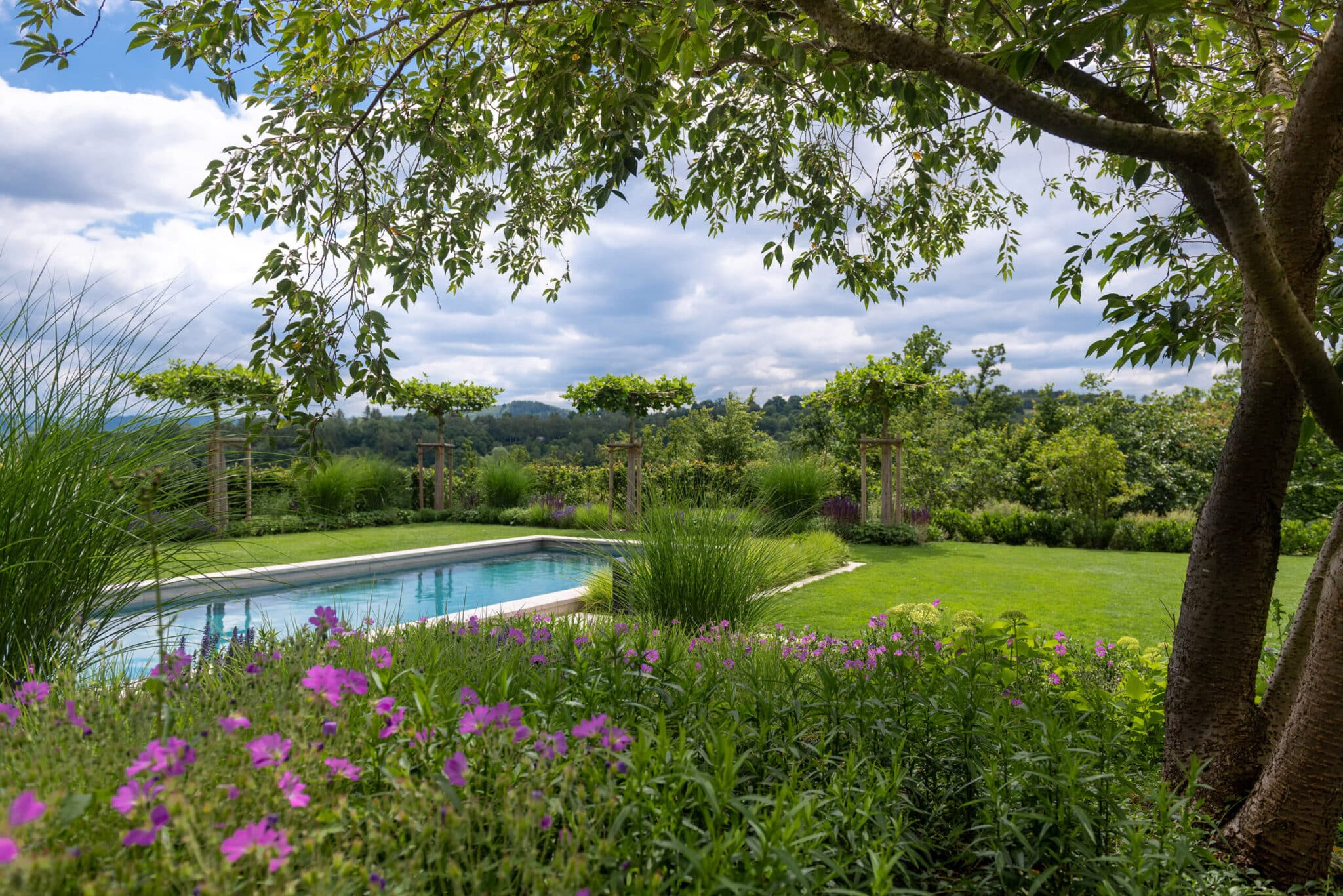 GvE Klute Schwimmbecken in einem Garten, umgeben von grünen Pflanzen und blühenden Blumen.