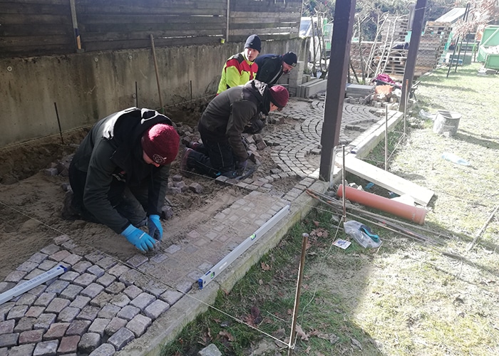 dav Auszubildende im Garten- und Landschaftsbau verlegen Pflastersteine auf einer Baustelle.
