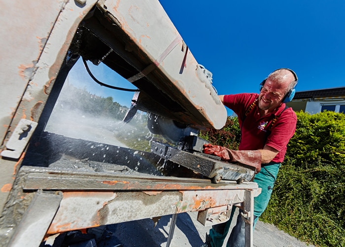 Job Quereinsteiger Klute Garten- und Lanschaftsbau Mann, der eine Steintrennmaschine im Garten- und Landschaftsbau bedient, mit Schutzkopfhörern und Wassernebel.